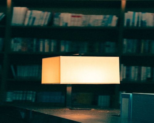A warm desk lamp illuminating a physical book in a dark room